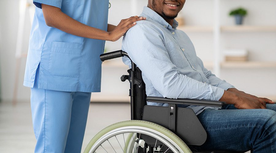 female-nurse-supporting-disabled-african-patient-on-a-wheelchair. Healthcare assistant vs Health support services.